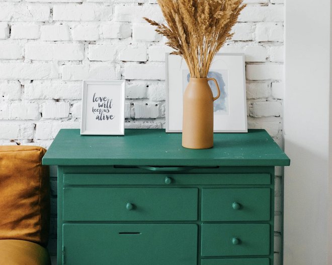 Green deskt holding two frames and a flower vase